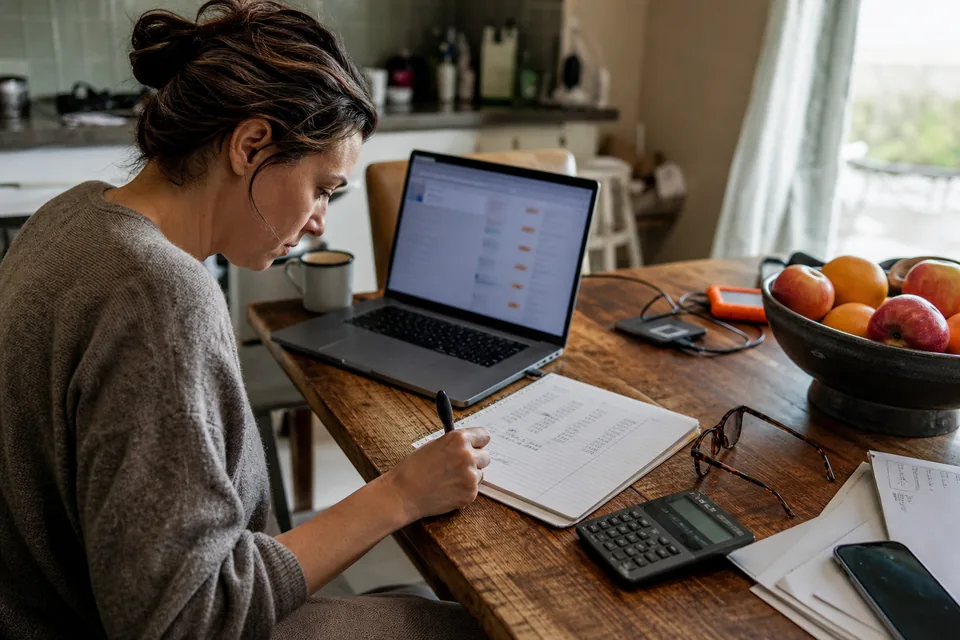 Domain seller working out list prices and marketplace commission on a notepad beside a laptop